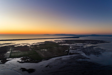 Obraz premium Aerial view of the Sado Estuary near the village of Carrasqueira, with a rice plantation, the Troia Peninsula and the Arrabida Mountain on the background at sunset, in Portugal.