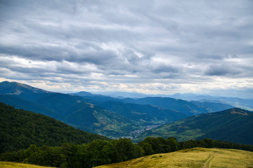 Fototapeta na wymiar Autumn Carpathian Mountains landscape with green trees on slope, cloudy sky, and village below, Rakhiv district, Svydovets, Transcarpathia, Ukraine