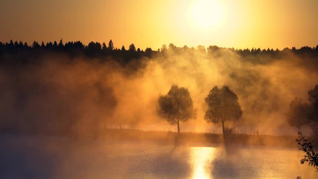 Orange sunrise on the lake or the river, morning mist at sunrise. Orange rays of the sun through the morning mist on the river