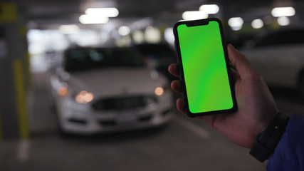 Lviv, Ukraine - May 19, 2018: Hands holding phone with vertical green screen in the background moving car flashing bonnet is raised man chroma key technology use mobile internet message smart sunlight