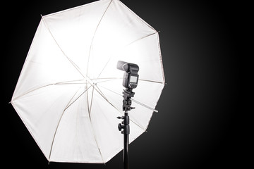 Studio stand with speedlight photo flash and white umbrella reflector