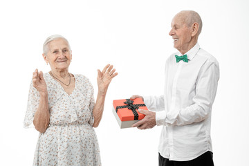 Happy elderly couple, senior man in white shirt present gift box to his old woman in white dress, celebrating birthday, isolated over white background