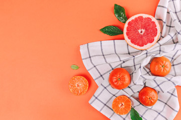 Fresh ripe mandarins and grapefruit with green leaves on white towel on orange background with space for text.