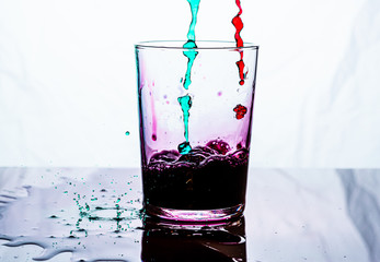 A glass being filled by pink and green liquid. White background.