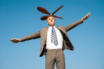 Businessman going airborne with helicopter propeller lifting him into sunny blue sky