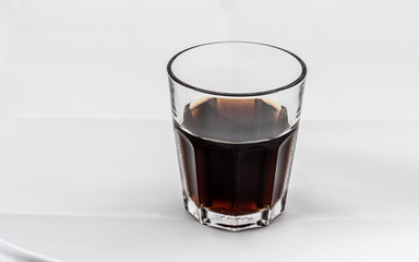 Dark brown drink in a glass on white background.