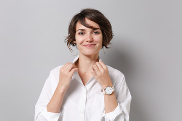 Obraz premium Smiling attractive young business woman in white shirt posing isolated on grey wall background studio portrait. Achievement career wealth business concept. Mock up copy space. Straightening collar.