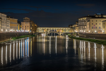 Ponte Vecchio in historical center downtown in Florence during sunrise with water reflections in Arno river