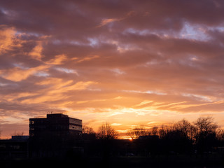 Silhouette of a building surrounded by trees at sunset, Warm glowing cloudy sky.