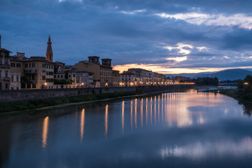 Florence old historical buildings reflecting in Arno river during a overcast sunrise morning with warm sun light