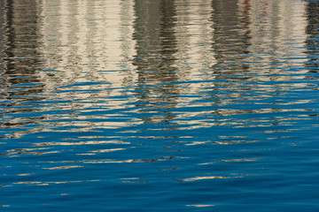 Water with small waves. Reflections of blue sky and buildings.
