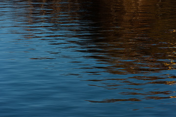 Water with small waves. Reflections of blue sky and buildings.