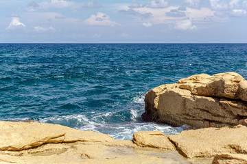 Fototapeta na wymiar Turquoise wave breaks on rocks of the Sliema coast, Malta. Wave and splashes on rocky Malta beach.
