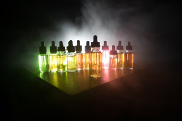 Smoke clouds and vape liquid bottles on dark background. Light effects. Useful as background or...