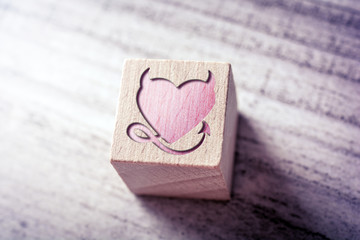 Red Naugthy Heart With Devil Horns And Tail Engraved On A Wooden Block On A Table