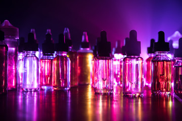Smoke clouds and vape liquid bottles on dark background. Light effects. Useful as background or...