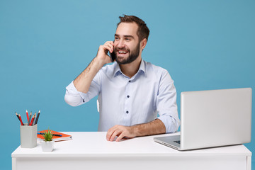 Smiling young bearded man in light shirt sit work at white desk with pc laptop isolated on pastel...
