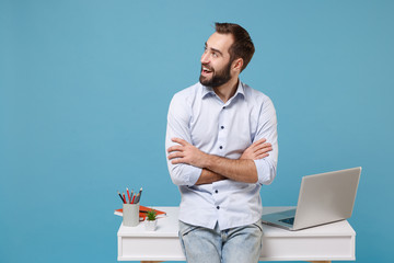 Cheerful young man in shirt work near white desk with pc laptop isolated on pastel blue background....