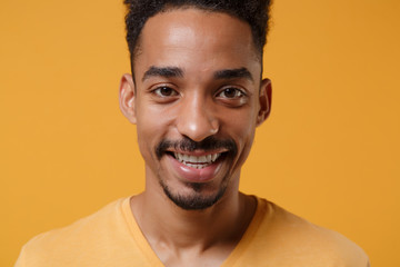 Obraz premium Close up of smiling young african american guy in casual t-shirt posing isolated on yellow orange wall background studio portrait. People emotion lifestyle concept. Mock up copy space. Looking camera.