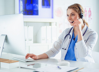 Young practitioner doctor working at the clinic reception desk, she is answering phone calls and scheduling appointments