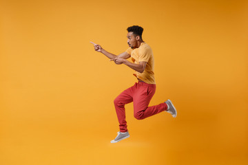 Fototapeta na wymiar Side view of young african american guy in casual clothes posing isolated on yellow orange background studio portrait. People lifestyle concept. Mock up copy space. Jumping point index fingers aside.