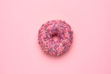Sweet pink donut with multicolored sprinkles on a pink background flat lay