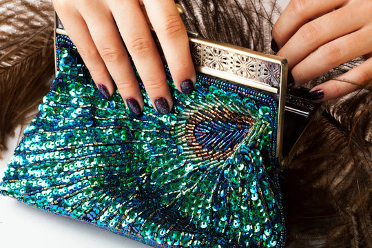 woman hands with shiny manicure holding little purse peacok feather, cosmetic and fashion people concept
