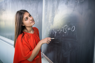 Pretty, young college student/young teacher writing on the chalkboard/blackboard during a math class