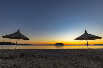 The beach at the Pakoštane with umbrellas and Kornati islands in the background after the sunset, Croatia