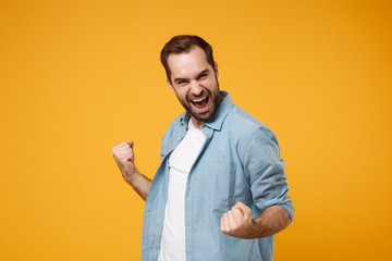 Happy young bearded man in casual blue shirt posing isolated on yellow orange wall background,...