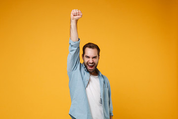 Joyful young bearded man in casual blue shirt posing isolated on yellow orange wall background,...