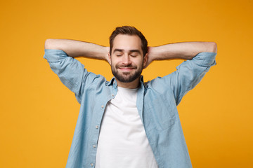 Relaxed young bearded man in casual blue shirt posing isolated on yellow orange background studio...