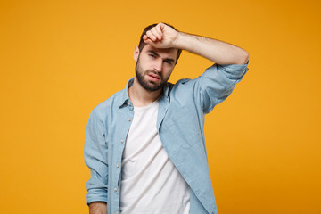 Tired exhausted young bearded man in casual blue shirt posing isolated on yellow orange wall background, studio portrait. People emotions lifestyle concept. Mock up copy space. Putting hand on head.