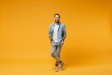 Smiling young bearded man in casual blue shirt posing isolated on yellow orange background, studio...