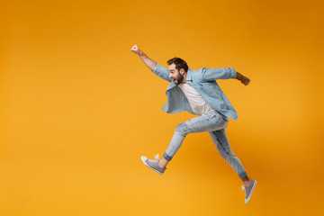 Fototapeta na wymiar Cheerful young bearded man in casual blue shirt posing isolated on yellow orange background studio portrait. People lifestyle concept. Mock up copy space. Jumping with outstretched hand like Superman.