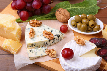 Assortment of cheese with fruits, grapes, nuts, glass with wine and cheese knife on a wooden serving tray.
