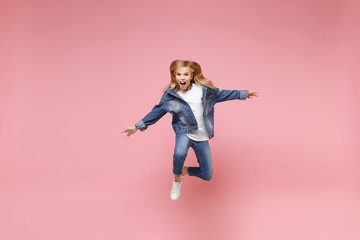 Crazy little blonde kid girl 12-13 years old in denim jacket isolated on pastel pink wall background children studio portrait. Childhood lifestyle concept. Mock up copy space. Jumping spreading hands.