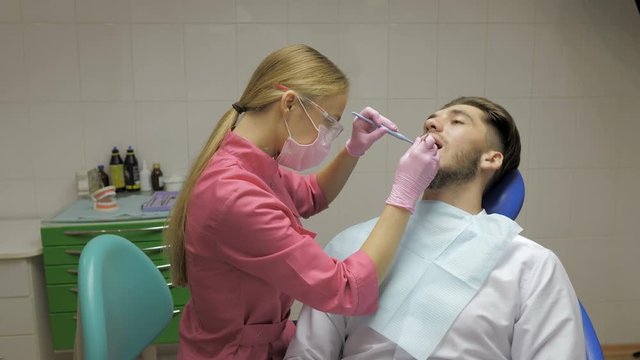 Female dentist with male patient doing the cleaning of the tooth in dentistry