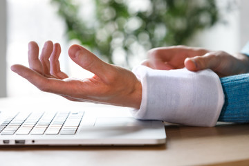 Close up of man applying cold compress to a his painful wrist caused by prolonged work on the computer, laptop. Carpal tunnel syndrome, arthritis, neurological disease concept. 