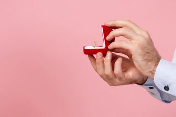 Close up cropped photo of male hold in hands red box with proposal ring isolated on pastel pink...