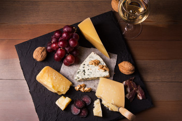 Assorted cheeses, nuts, grapes, fruits, smoked meat and a glass of wine on a serving table. Dark and Moody style. Free space for text.