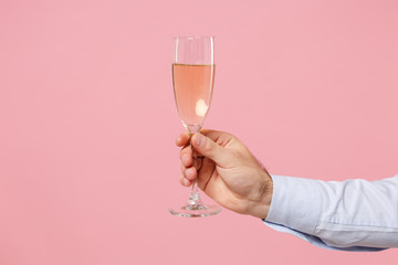 Close up cropped photo of male hold in hand glass of champagne isolated on pastel pink wall background. Copy space advertising mock up. Valentine's Day Women's Day birthday holiday party concept.