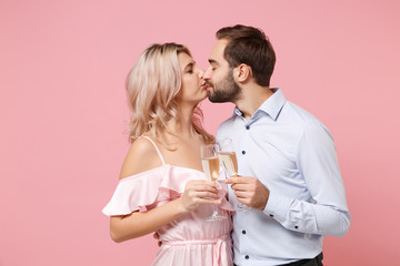 Young couple two guy girl in party outfit celebrating posing isolated on pastel pink background. People lifestyle Valentine's Day Women's Day birthday holiday concept. Hold glass of champagne kissing.