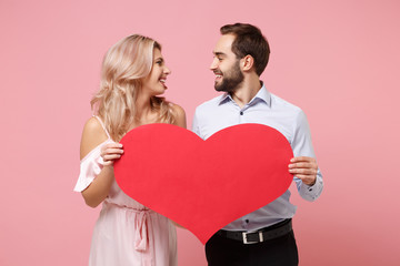 Fototapeta na wymiar Smiling young couple two guy girl in party outfit celebrating posing isolated on pink background. People lifestyle Valentine's Day, Women's Day birthday holiday concept. Hold empty blank red heart.