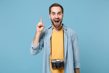 Excited traveler tourist man in yellow summer clothes with photo camera isolated on blue background. Male passenger traveling abroad on weekends. Air flight journey Hold finger up with great new idea.