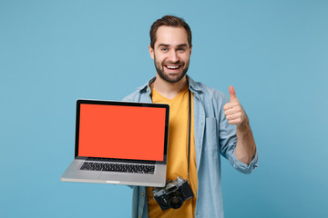 Traveler tourist man in casual clothes with photo camera isolated on blue background. Passenger traveling on weekends. Air flight journey. Hold laptop pc computer with blank screen, showing thumb up.