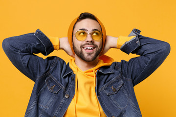 Pensive young hipster guy in fashion jeans denim clothes posing isolated on yellow orange background studio portrait. People lifestyle concept. Mock up copy space. Looking up with hands behind head.