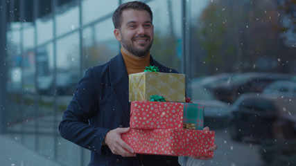 Smiling young attractive man walking with Christmas presents boxes portrait handsome shopping look...