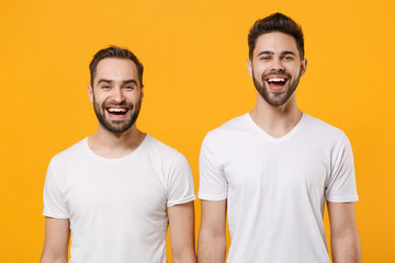 Laughing young men guys friends in white blank empty t-shirts posing isolated on yellow orange background studio portrait. People sincere emotions lifestyle concept. Mock up copy space Looking camera.