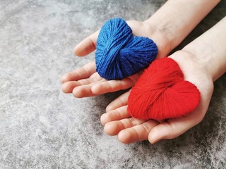 The girl presents two abstract knitted hearts in her hands. Valentine's Day postcard.